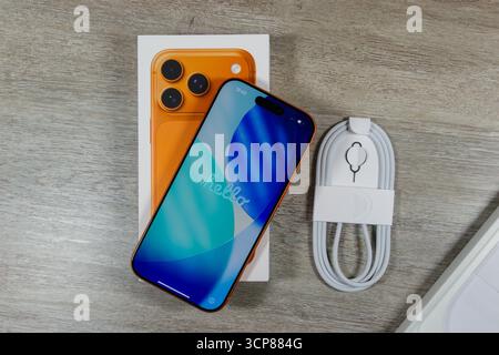 New iPhone 17 Pro smartphone with orange back and blue screen displaying 'hello', resting on its box with charging cable on wooden surface Stock Photo