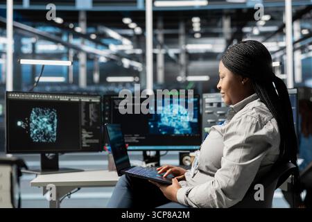 Smiling server hub staff member looks at data analysis graph to reduce infrastructure failure. Jolly data center system administrator looks at AI visualization dashboard to pinpoint equipment glitches Stock Photo