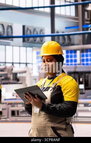 High tech manufacturing engineer develops robotic workflows with software on tablet. African american automation specialist monitors and upgrades industrial plant machinery through digital interface. Stock Photo