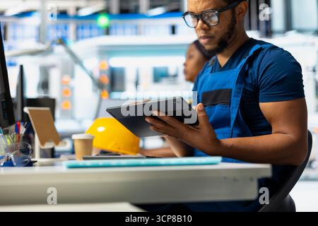 Black technician in solar panel facility reviewing photovoltaic system performance on tablet. Male employee analyzing production line to optimize efficiency in industrial manufacturing plant. Stock Photo