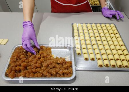 Person wearing purple gloves preparing rolled pastries with a tray of pineapple filling in an open fronted kitchen street food malacca malaysia Stock Photo