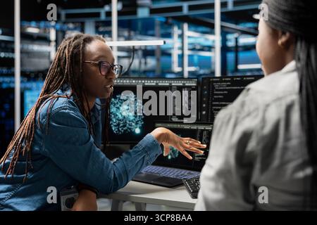 Data center team leader oversees engineer using artificial intelligence visualization tools to identify bugs. Server hub manager supervises worker using AI generated insights to detect hardware errors Stock Photo