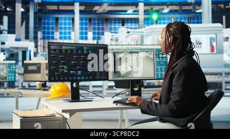 Photovoltaics factory programmer coding on PC to improve solar panels efficiency. African american software developer working in solar panels manufacturing plant, doing research, camera A Stock Photo
