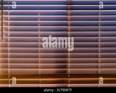 The sun is shining through faux wood Venetian blinds hanging on a window Stock Photo