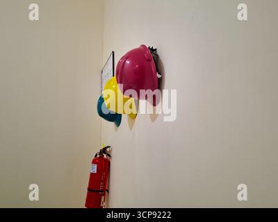 Colorful Hard Hats Hanging on a Wall Adjacent to a Fire Extinguisher in a Workplace Stock Photo