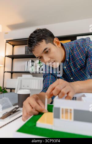 A young architect works on house design plans at his desk, focusing on drawings and scale models. The scene conveys creativity, dedication, and precis Stock Photo