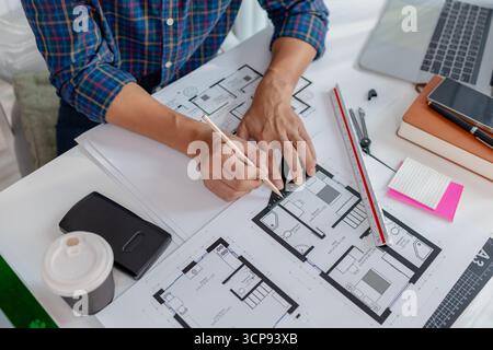 A young male architect is working with blueprints at his desk, using rulers and drawing tools to refine details. He appears focused and engaged, balan Stock Photo