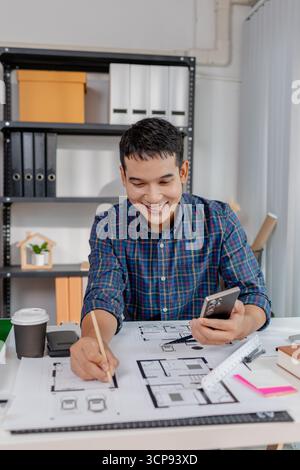 A young male architect is working with blueprints at his desk, using rulers and drawing tools to refine details. He appears focused and engaged, balan Stock Photo