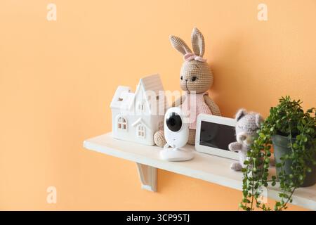 Shelf with baby monitor, toys and plant on orange wall in children's room Stock Photo