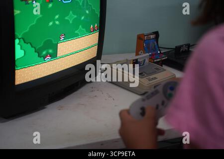 A nostalgic image of a vintage Super Nintendo (SNES) and controller on a desk. A girl plays a classic game on an old CRT TV, capturing 90s gaming. Stock Photo
