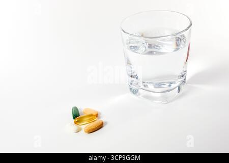 A daily dose of various colorful pills, capsules, and vitamins with a glass of water. A concept for taking medication, a daily health routine, and fol Stock Photo