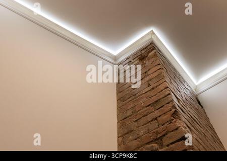 A contemporary interior featuring an exposed brick pillar rising from a white wall, softly lit by indirect cove lighting. Rugged brick contrasts with Stock Photo