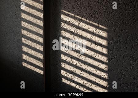 A warm interior scene features diagonal shadows from window blinds across a textured wall, creating a calm, contemplative mood. Ideal for home or offi Stock Photo