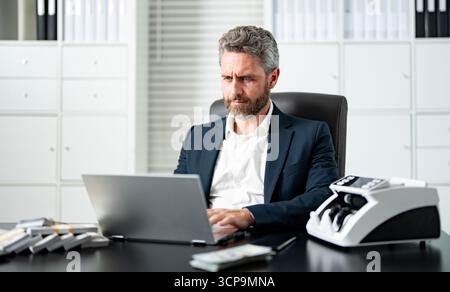 Businessman counting money at his office desk. Banker handling cash and bills in a corporate setting. Accountant organizing dollars and banknotes for Stock Photo