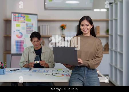UI UX Design Team. Young woman smiling while holding laptop in modern creative office. Stock Photo