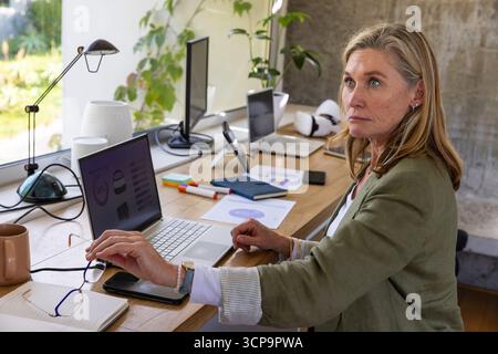 Senior woman analyzing charts on laptop at home office desk with vr headset, copy space Stock Photo