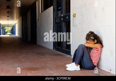 Girl child sitting on red brick corridor floor in covered hallway wearing striped shirt, copy space Stock Photo