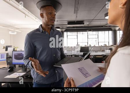 Diverse coworkers analyzing bar graph data with laptop, charts in open plan office Stock Photo