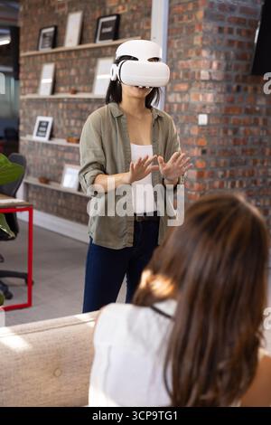 Asian coworkers wearing VR headset and using tablet at office desk with ...