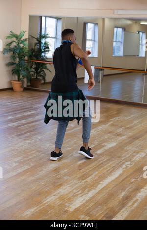 African American man practicing dance moves in studio with mirrored wall, barre and plants Stock Photo