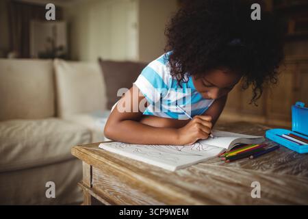 African American girl child leaning over coffee table at home coloring pages with colored pencils Stock Photo