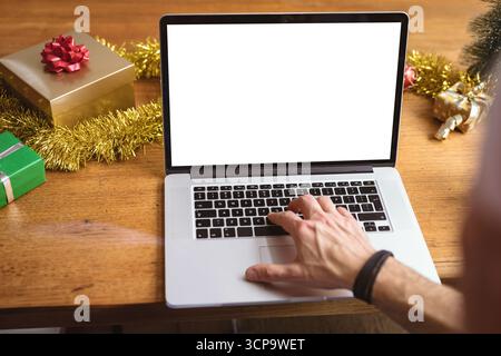 Man reaching toward silver laptop on festive table at home with gift boxes and tinsel garland Stock Photo