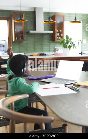 African American boy studying using laptop with headset at dining table in kitchen, copy space Stock Photo