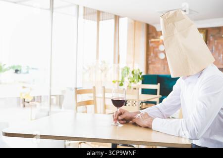 Man sitting at table in cafe holding wine glass with paper bag over head, copy space Stock Photo