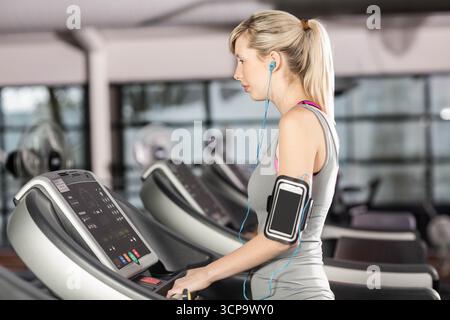 Woman running on treadmill in gym wearing sportswear and using smartphone armband, copy space Stock Photo