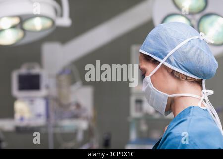 Mid adult female nurse monitoring vitals on monitors under surgical lights in OR, copy space Stock Photo