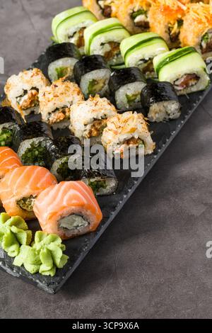 Assorted sushi rolls served on a slate plate with wasabi, soy sauce, and ginger Stock Photo