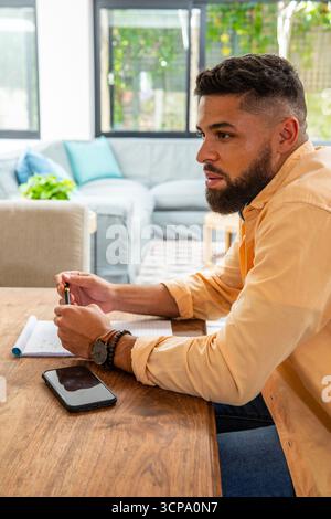 Man scribbling in notebook while leaning on wooden table at home with smartphone Stock Photo