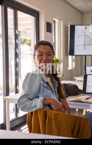 Chinese woman studying with laptop and notebook at bright study room desk with graph display Stock Photo