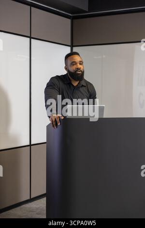 Mid-adult african american man in shirt speaking at podium using laptop in conference room Stock Photo