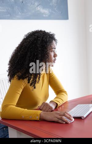 African american woman sitting at desk in home office using computer mouse under painting Stock Photo
