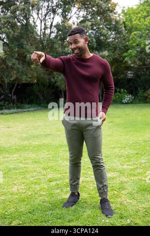 African american man standing on home lawn pointing beyond frame in maroon sweater Stock Photo