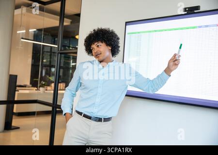African american man presenting spreadsheet on screen in office holding marker leaning near wall Stock Photo