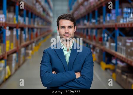 Male warehouse manager is standing in aisle lined with racks of inventory under fluorescent lights Stock Photo