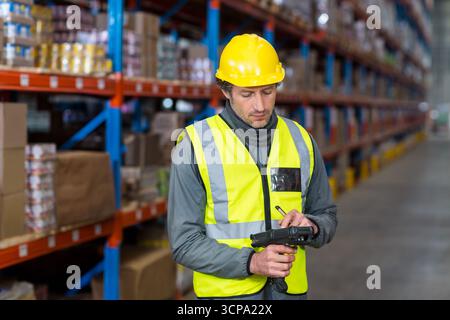 Warehouse worker wearing high-vis vest scanning boxes using scanner between metal shelving racks Stock Photo