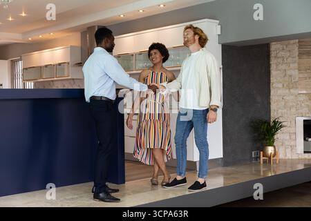 African american agent in suit shaking hands with homebuyer couple in kitchen Stock Photo