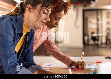 Diverse female coworkers leaning over table planning ideas in office with sticky notes Stock Photo