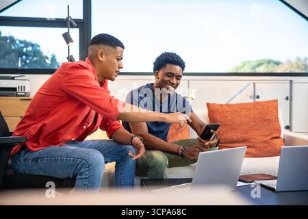 Diverse coworkers collaborating on laptops and smartphone in office lounge on sofa with tablet Stock Photo