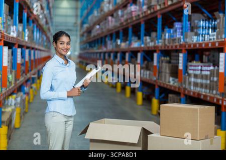 Inventory supervisor checking clipboard scanning boxes on aisle flanked by racks with yellow posts Stock Photo