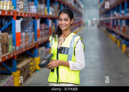 Asian female worker scanning boxes on pallets with scanner next to racks in warehouse under lights Stock Photo