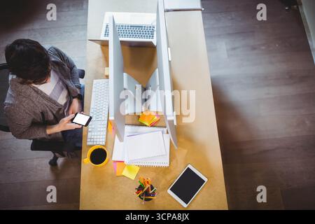 Male office worker checking smartphone while sitting at office desk with monitors, copy space Stock Photo