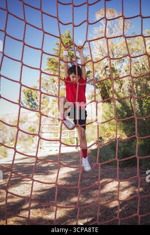 School-aged boy climbing red rope net on obstacle course wearing sweat wristband, white shoes Stock Photo