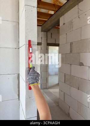 A metal hand level is applied to a wall in a new building. Measuring the evenness of the wall surface. The hand holds the level on the wall. Measuring Stock Photo