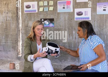 Diverse colleagues examining vr headset in workshop using tablet, charts and sticky notes Stock Photo
