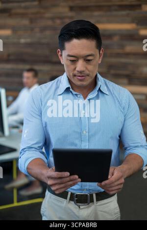 Diverse coworkers standing and sitting at desks in modern office using tablet and desktop computers Stock Photo