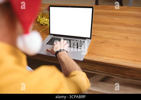 Mature adult man typing on laptop at home office table with tinsel, Santa hat, copy space Stock Photo